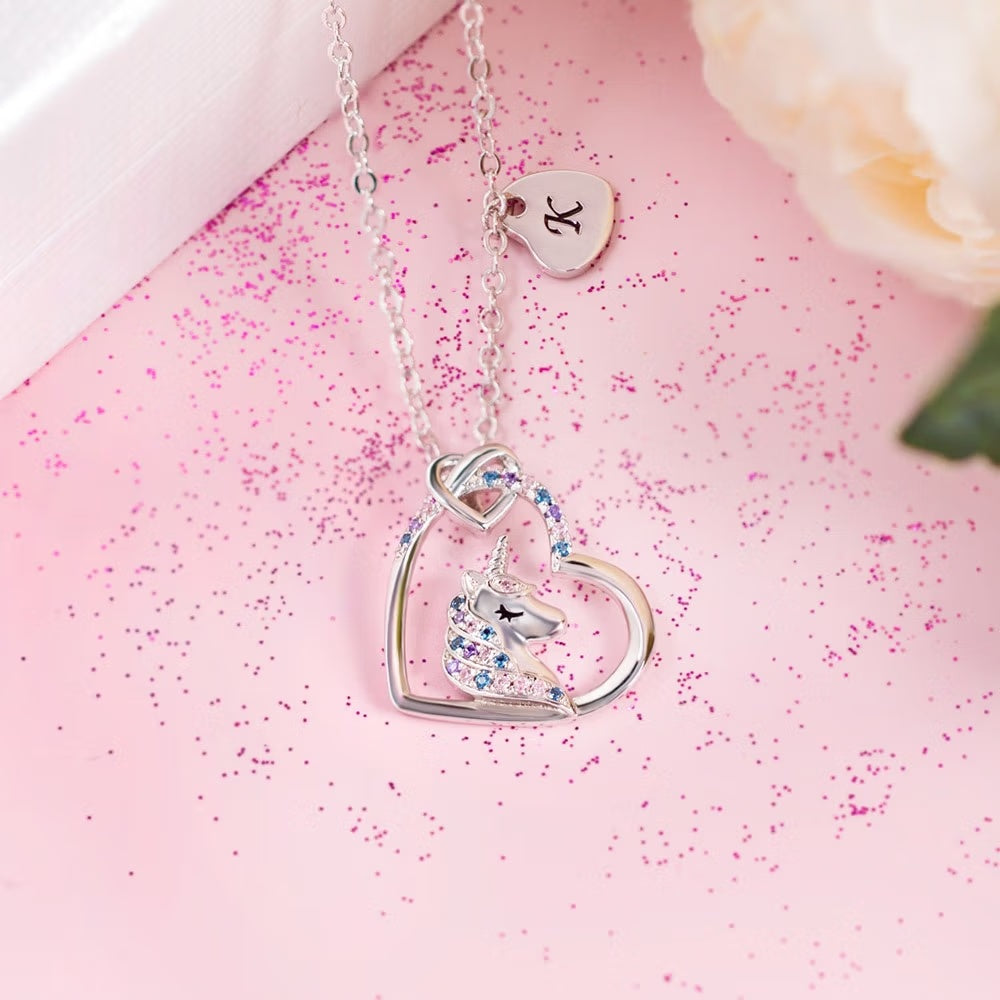 Silver unicorn heart pendant necklace with separate initial charm on pink background