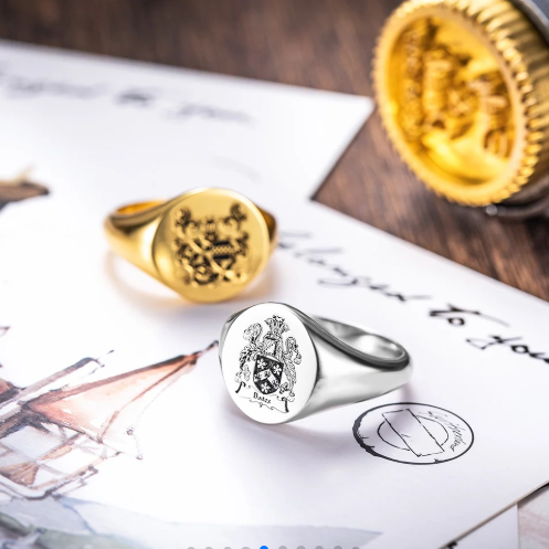 Custom engraved gold and silver signet rings displayed with family crest artwork