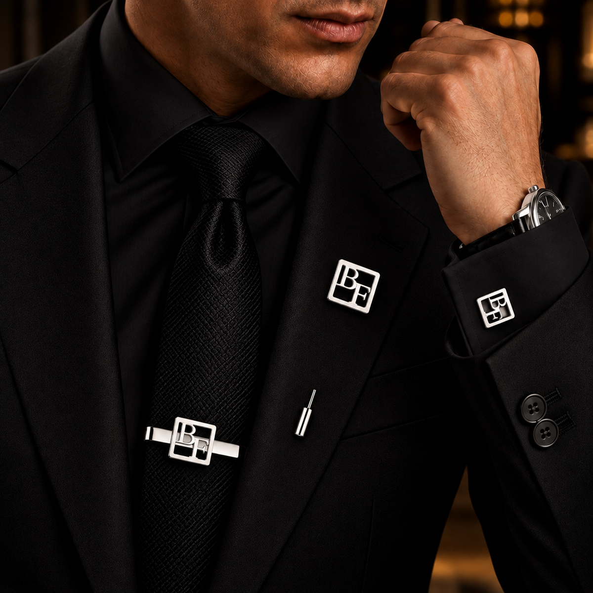 Man wearing personalized silver geometric monogram cufflinks, matching tie bar and lapel pin with a black suit