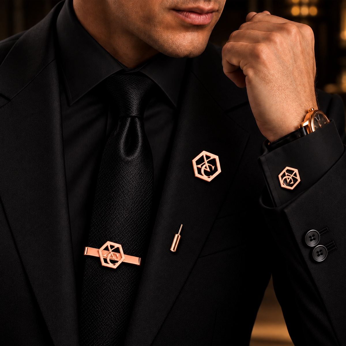 Man wearing rose gold geometric monogram cufflinks, matching tie bar and lapel pin with a black suit