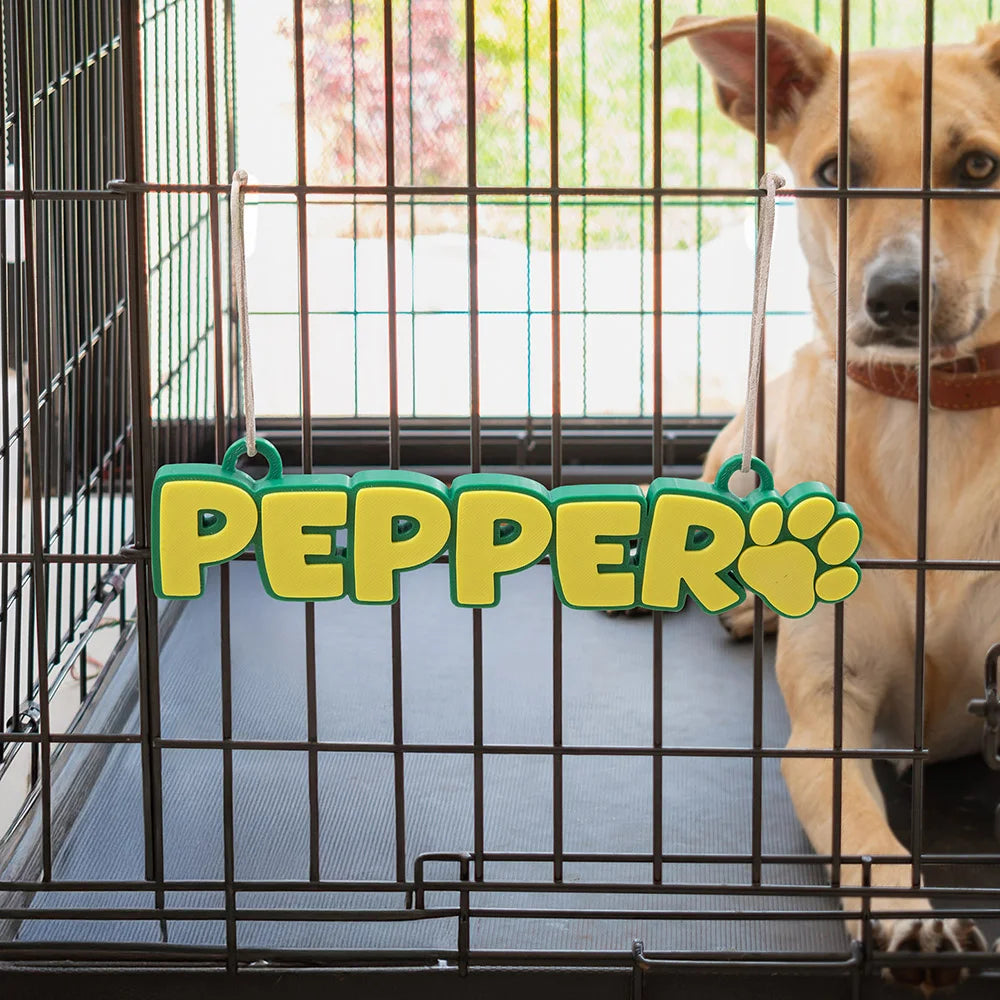 Personalized dog name tag 'PEPPER' with paw print, hanging on crate, custom pet gift