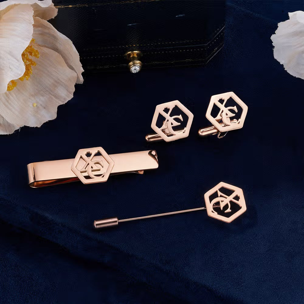 Rose gold geometric monogram cufflinks, tie bar and lapel pin set displayed on navy blue fabric