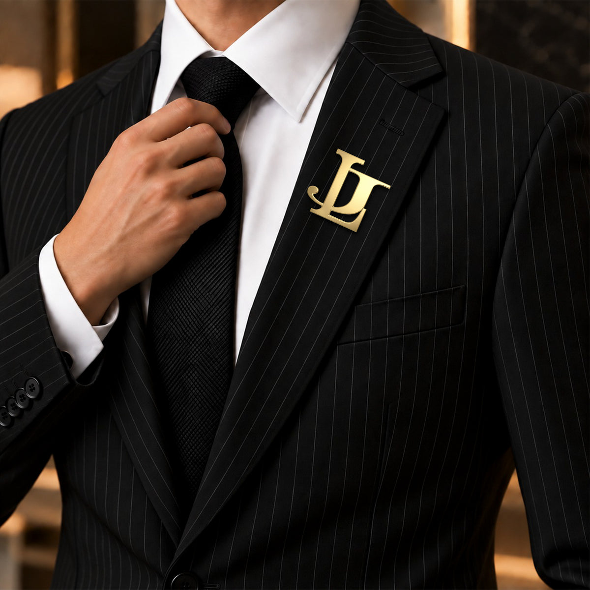 Custom gold two-initial monogram lapel pin worn on a black pinstripe suit with a white shirt.