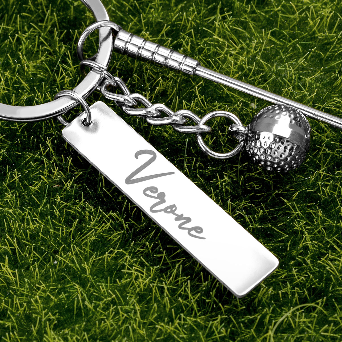 Close-up of personalized golf keychain with engraved name tag, golf club and ball charms on grass