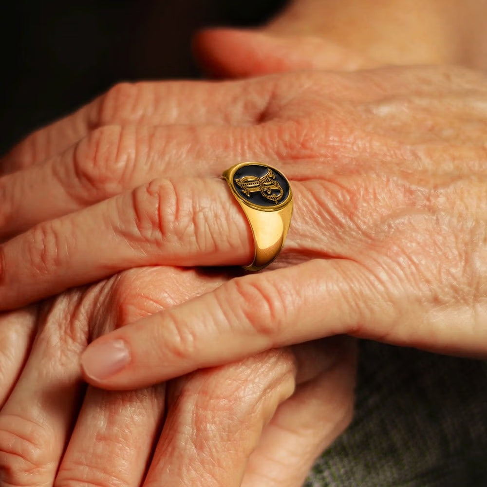 Gold tone personalized initials signet ring with black engraved face shown on a hand.