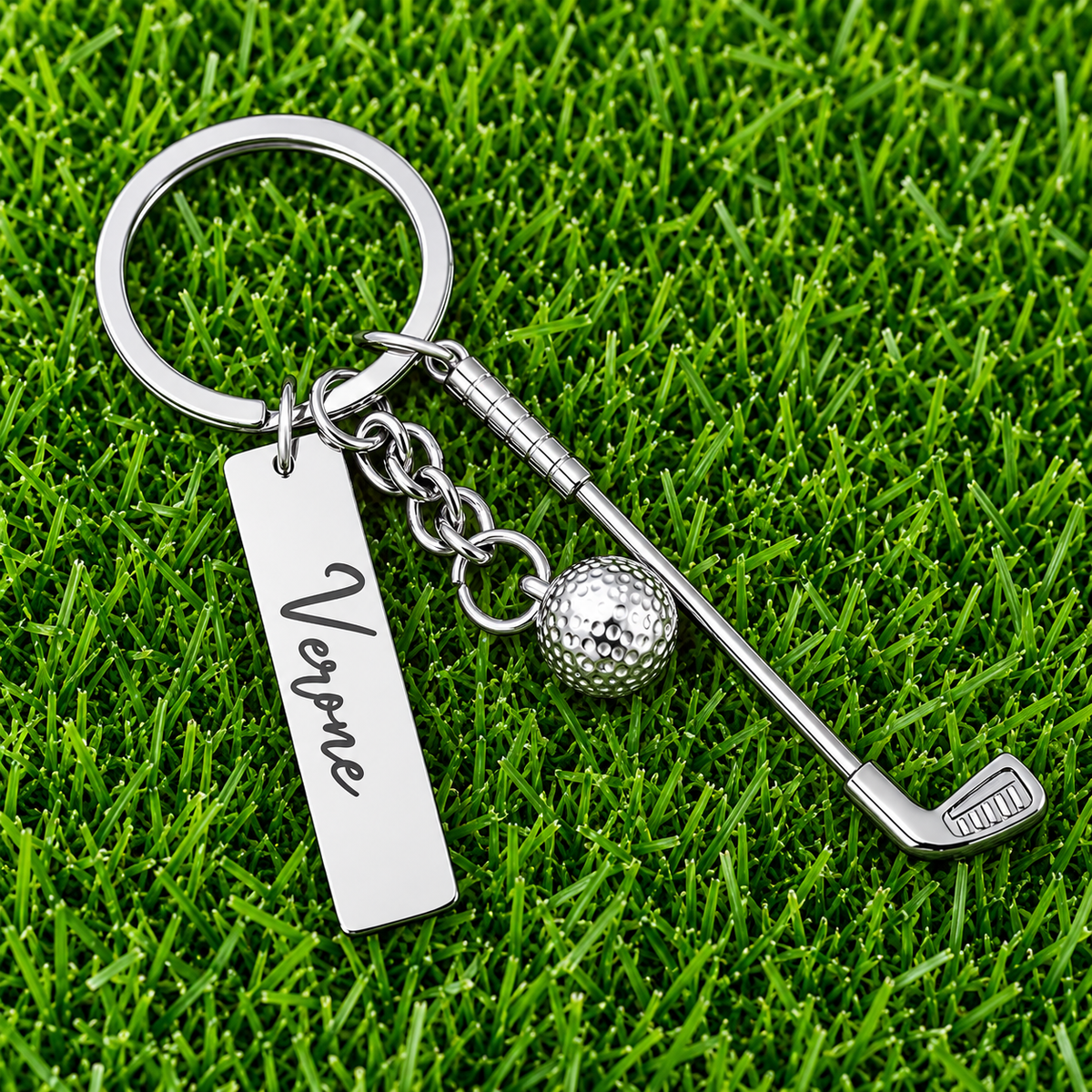 Custom name golf keychain with miniature golf club and ball charms displayed on green grass