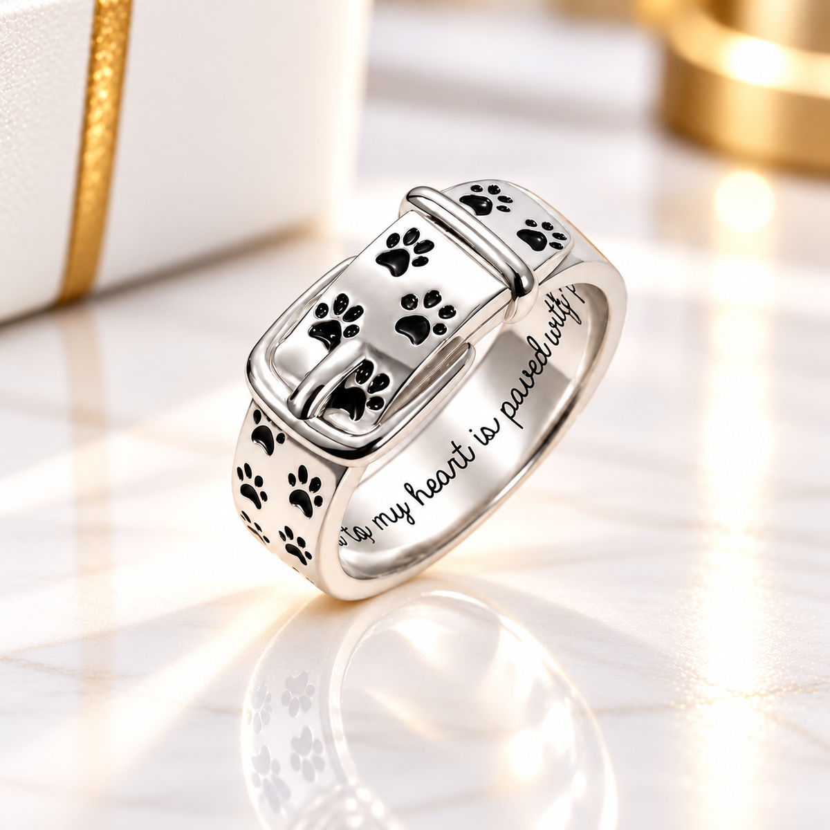 Personalized 925 sterling silver pet paw print buckle ring featuring black paw print details and an engraved message inside the band, displayed on an elegant white marble background with gold accents.