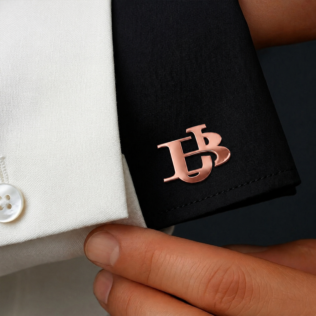 Rose gold interlocking initials cufflink on a black shirt cuff beside a white dress shirt cuff.