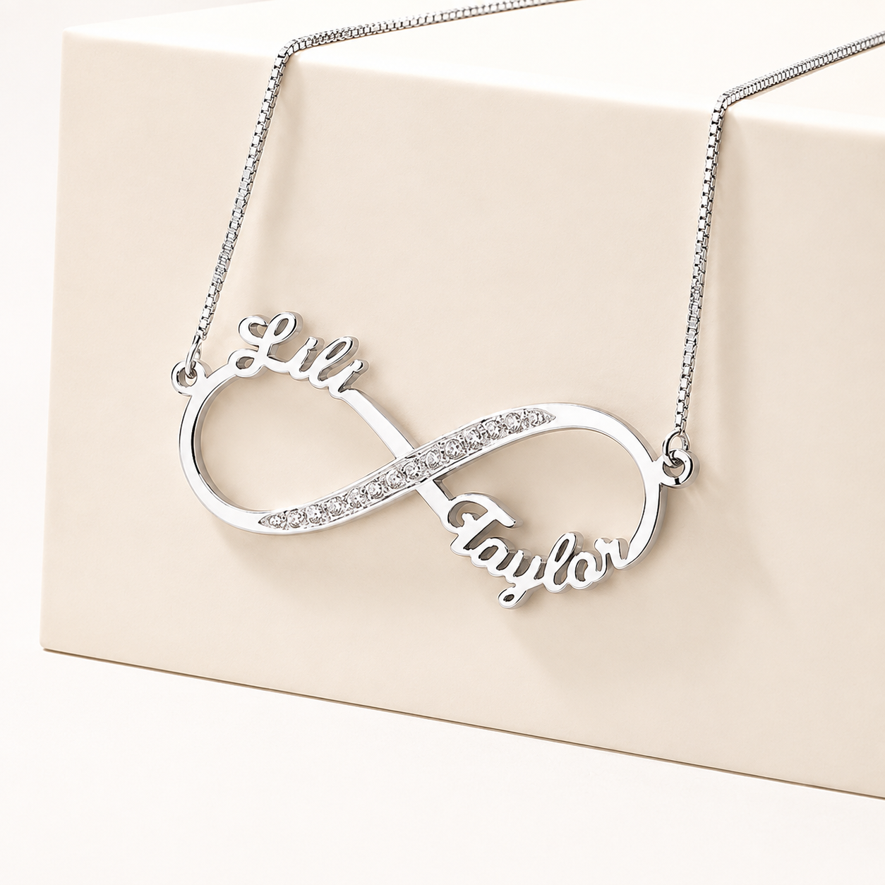 Silver two name infinity necklace displayed on cream jewelry box
