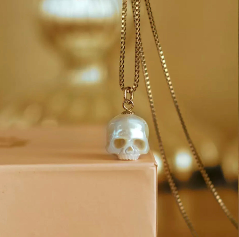 Translucent skull pendant on a box chain, poised on a peach-colored box with a softly blurred background.
