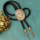 Personalized bolo tie with gold initial J, braided black cord, and decorative ends, styled with dried flowers