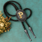 Custom bolo tie with gold letter P, braided leather cord, and engraved silver tips, styled with dried flowers.