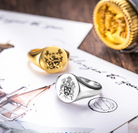 Custom engraved gold and silver signet rings displayed with family crest artwork