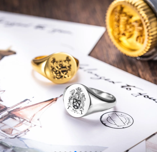 Custom engraved gold and silver signet rings displayed with family crest artwork