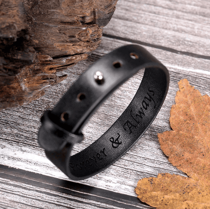 Black leather bracelet with 'Forever & Always' engraving, showcased on a textured wooden surface with autumn leaves.