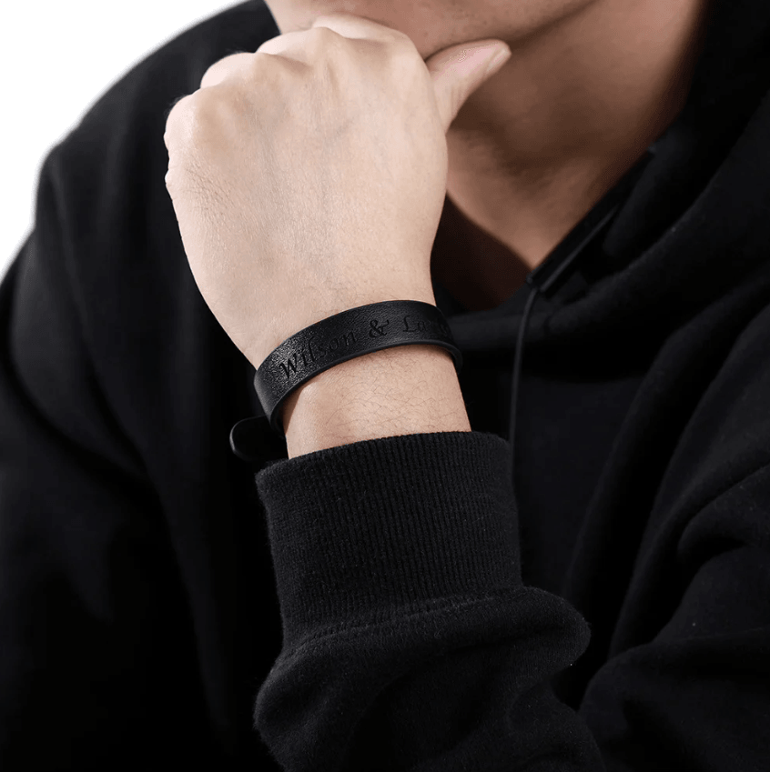 Man wearing a custom black leather bracelet engraved with personal message, styled with a casual black hoodie.