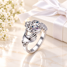 Personalized 925 sterling silver Claddagh ring with Celtic knot design, heart and crown detailing, and birthstones, displayed on luxury cream marble beside a white gift box with satin ribbon, meaningful Irish jewelry gift for love, loyalty, and friendship.