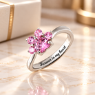 Personalized silver paw print birthstone ring with sparkling pink gemstones and Forever in my heart engraving, displayed on a soft ivory marble background.