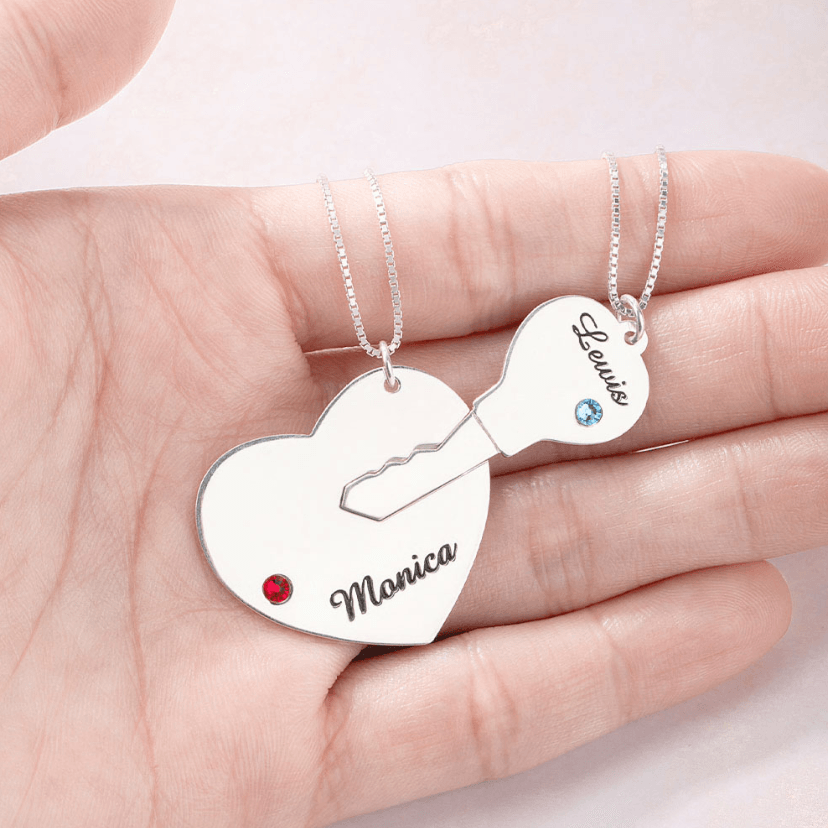 Close-up of personalized "Key to My Heart" couple necklace set with custom names Monica and Lewis and birthstones in sterling silver. Heart and key pendants.