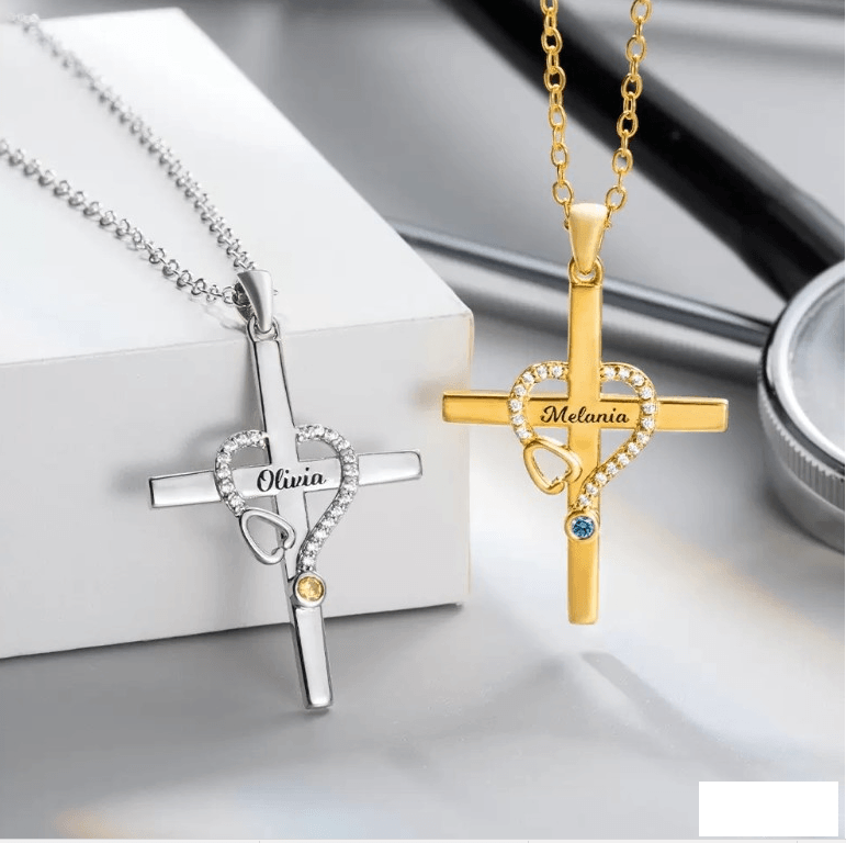 Two personalized cross necklaces with a stethoscope forming a heart around the names Olivia and Melania, each with a birthstone, one silver, one gold.