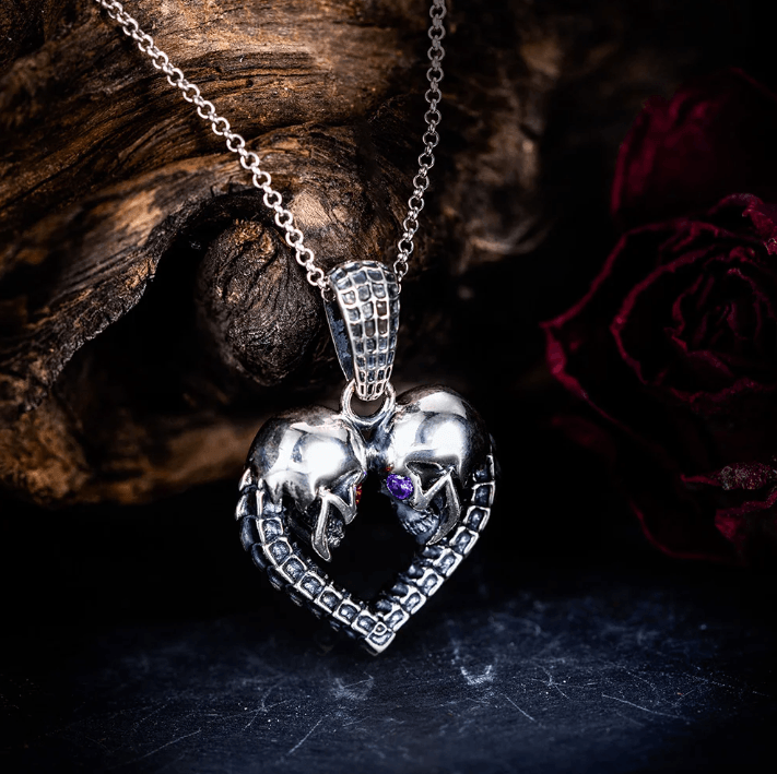 Gothic silver heart necklace with skull details and gemstone eyes, against a dark backdrop.