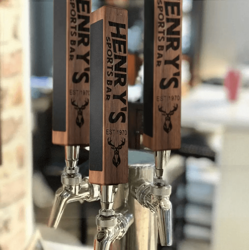 Custom beer tap handles with personalized engraving and chalkboard decals displayed on a kegerator at Henry's Sports Bar, featuring a deer logo.