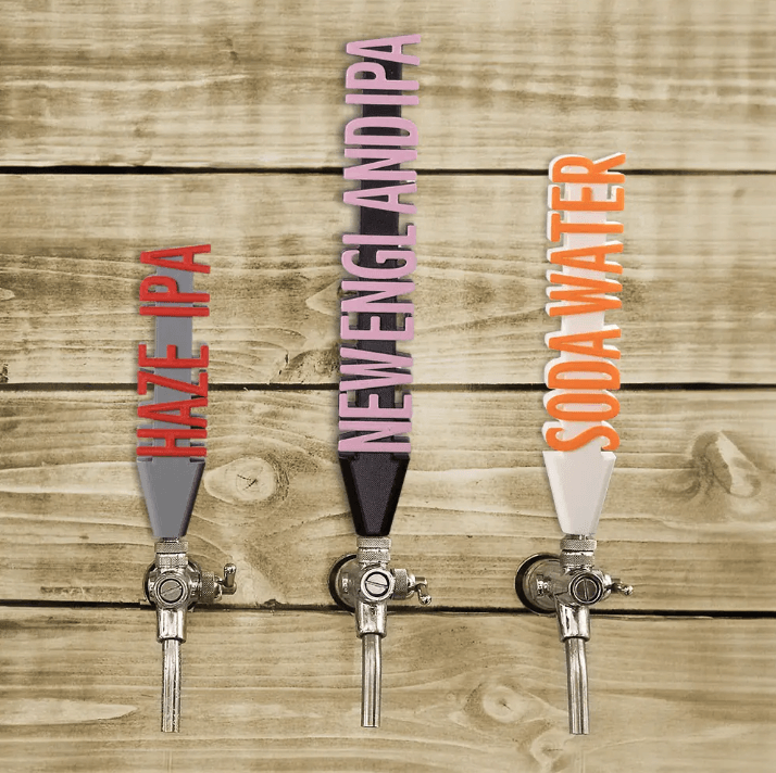 Three beer taps with custom 3D printed handles for 'HAZE IPA', 'NEW ENGLAND IPA', and 'SODA WATER' mounted on a wooden wall.