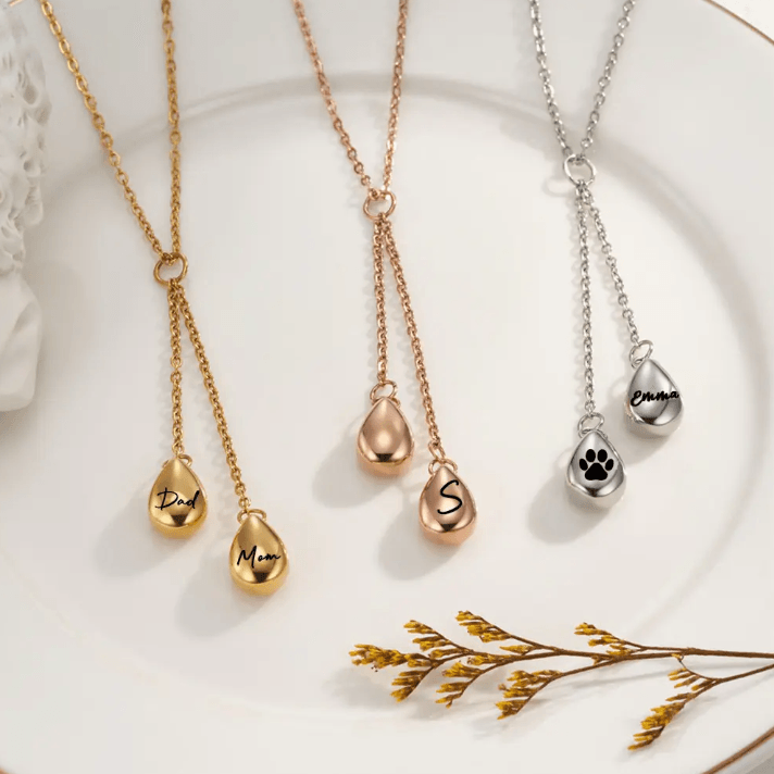Assortment of personalized cremation urn necklaces in gold, rose gold, and silver finishes, engraved with names and symbols