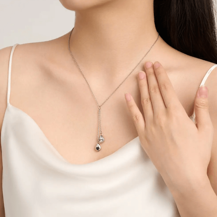 Silver necklace with a teardrop pendant on a woman's neck, her hand gently touching the chain.