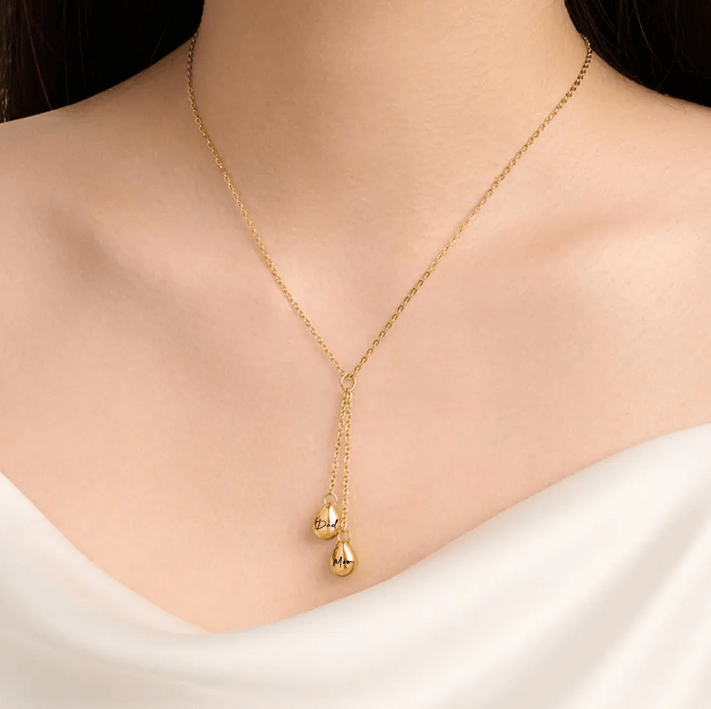 Elegant gold Y-shaped necklace with engraved 'Dad' and 'Mom' teardrop pendants, displayed on a woman's neck.