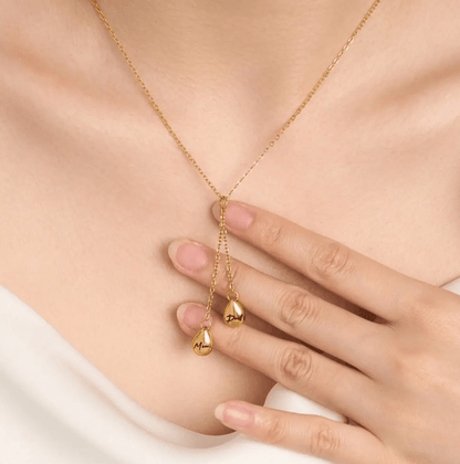 Gold Y-shaped necklace with 'Dad' and 'Mom' engraved teardrop pendants, worn by a woman touching the jewelry.