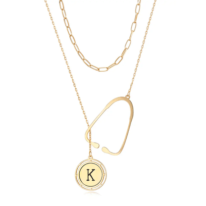 Layered gold necklace with a stethoscope pendant and a custom initial charm, displayed against a white background.