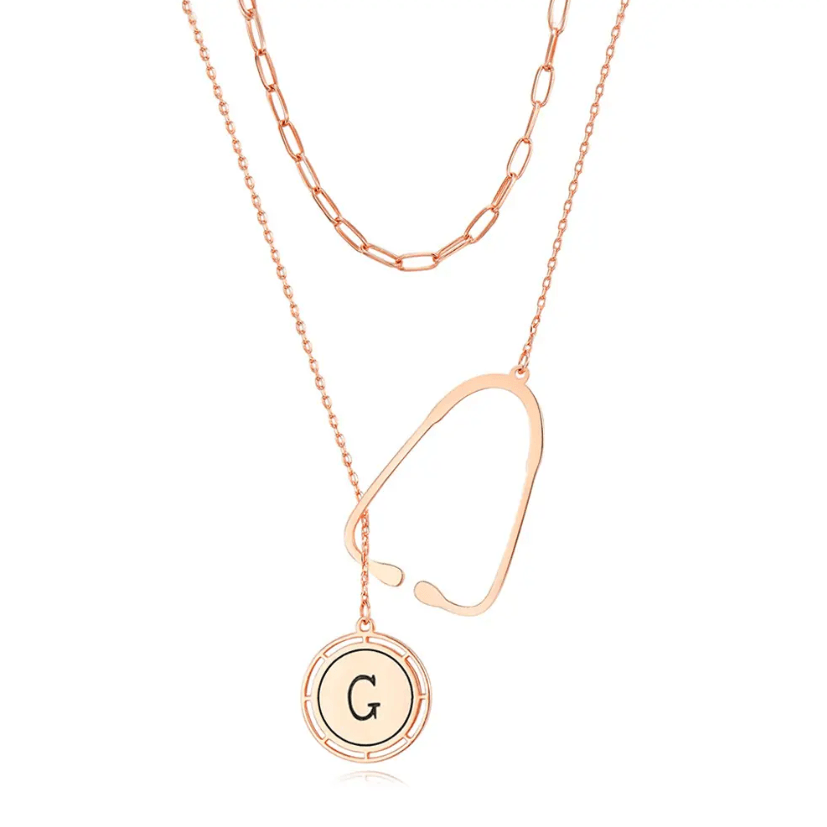 Layered rose gold necklace with a stethoscope pendant and a custom initial charm, displayed against a white background.