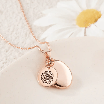 Rose Gold Personalized Birth Flower Necklace with Oval Photo Locket, featuring a flower engraving, displayed on a light surface with a white daisy in the background.