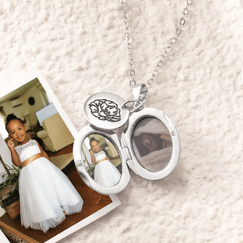 Personalized Silver Birth Flower Necklace with Oval Photo Locket, featuring a flower engraving and holding two photos, displayed with a photo of a young girl in a white dress.