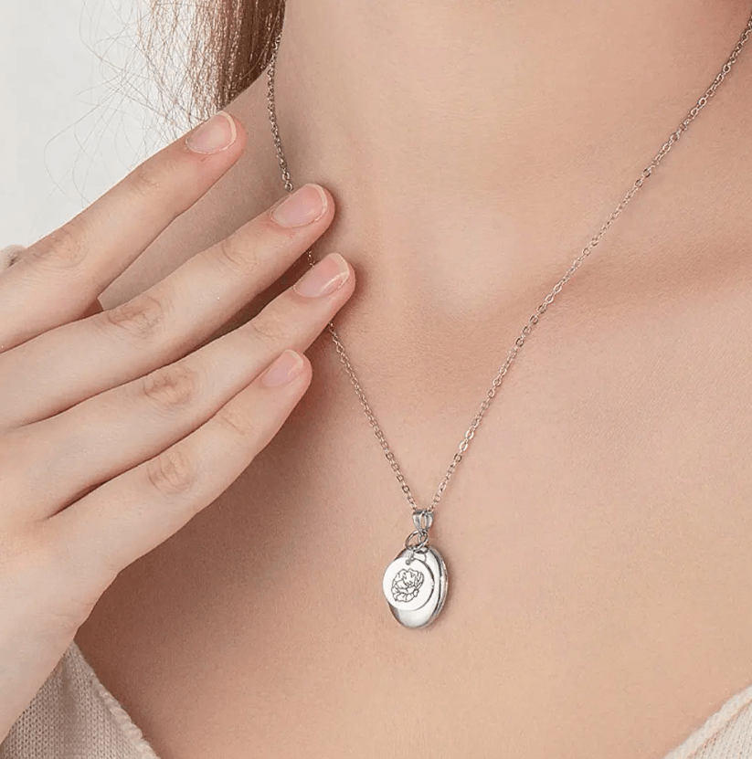 Close-up of a woman wearing a Silver Personalized Birth Flower Necklace with Oval Photo Locket, featuring a detailed flower engraving, against a light background.