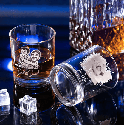 Two custom engraved whiskey glasses, one with "Dad & Daniel" photo and one with "Happy Father's Day, Love Evelyn" message, placed next to ice cubes and a decanter.