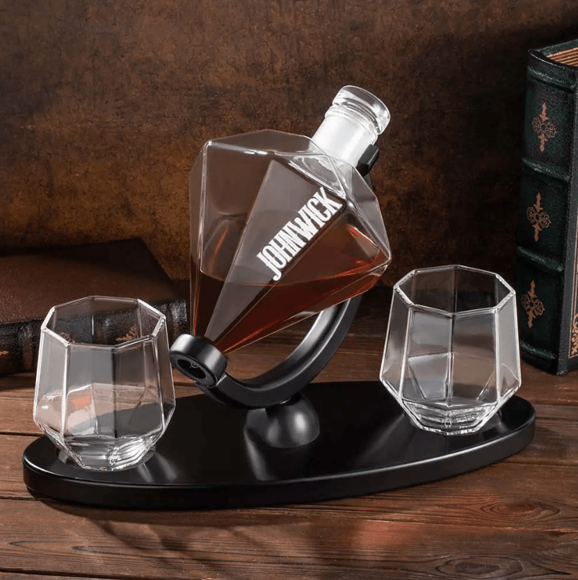 Custom engraved diamond-shaped whiskey decanter labeled 'John Wick' with two geometric glasses on a sleek black stand, placed on a wooden table.