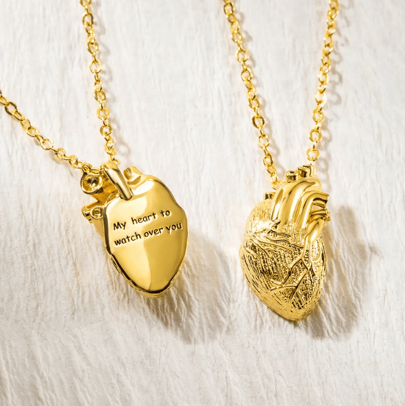 Two gold heart-shaped necklaces; one smooth with an inscription, and one textured like a human heart, on a textured white background.