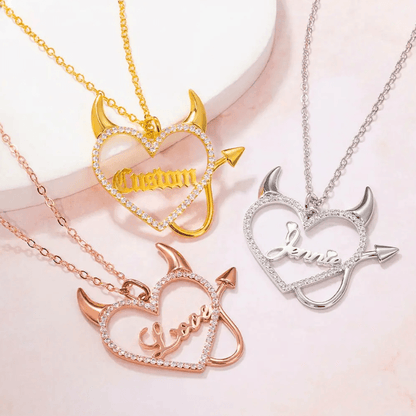 Three heart-shaped necklaces with devil horns and tail, featuring custom names or words, in gold, rose gold, and silver finishes, adorned with sparkling stones.