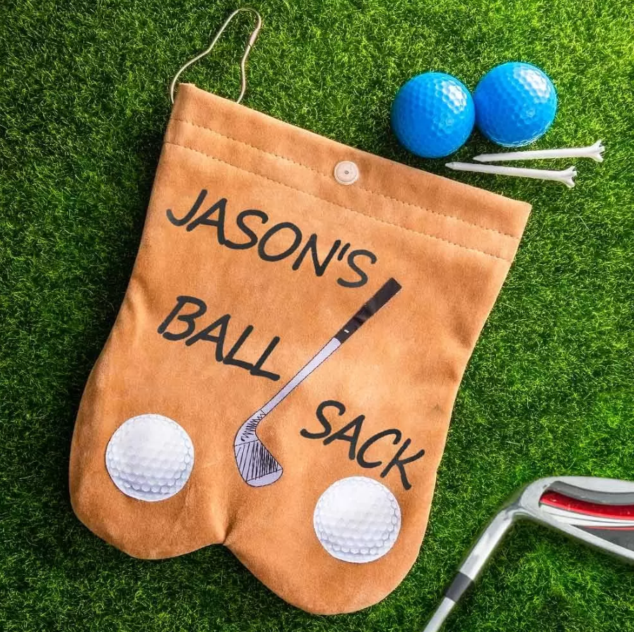 Custom tan flannelette golf ball sack labeled 'Jason's Ball Sack' on grass, with golf balls, tees, and a club nearby, showcasing a humorous and personalized design.