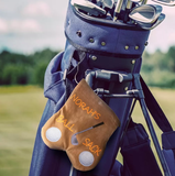 Norah's Ball Sack' attached to a navy blue golf bag, set against a serene golf course backdrop, highlighting a tailored, handy golf accessory.