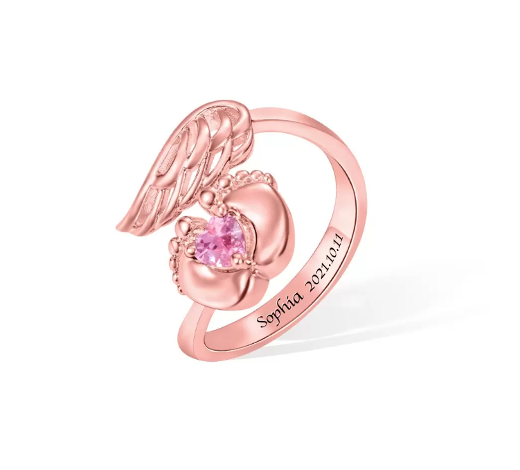 A rose gold -toned memorial ring with a heart-shaped stone cradled by feet, angel wings on top, and an inscription "Sophia 2021.10.11".