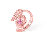 A rose gold -toned memorial ring with a heart-shaped stone cradled by feet, angel wings on top, and an inscription "Sophia 2021.10.11".