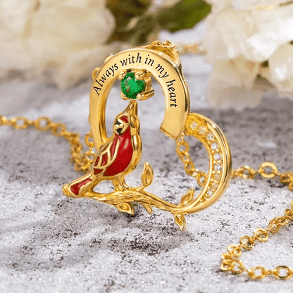Gold 'Always with in my heart' cardinal necklace with green gemstone on snowy surface.