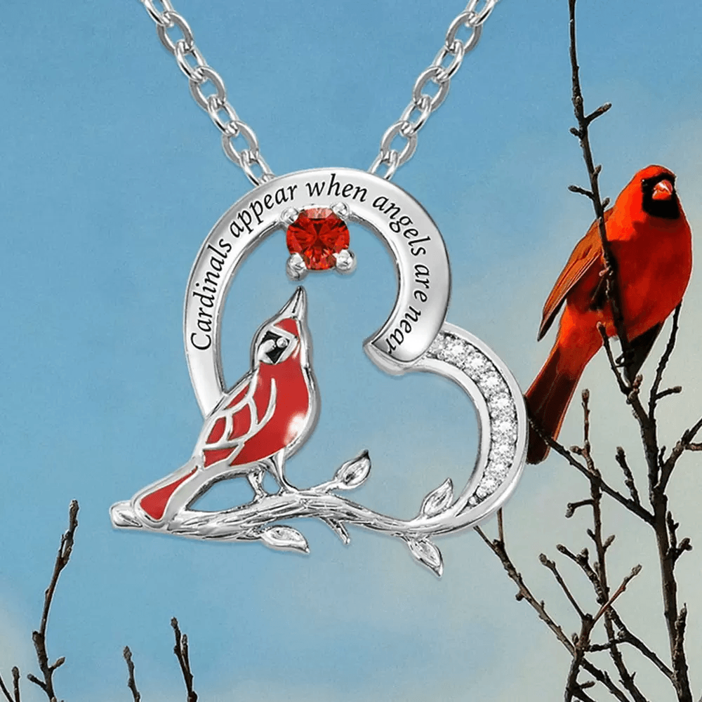 Engraved silver cardinal pendant with a chain, featuring a red gemstone, against a blue sky backdrop.