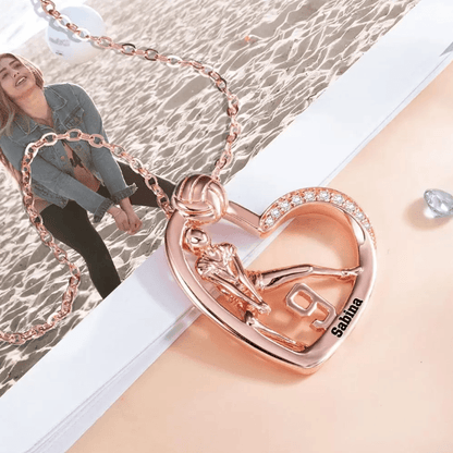 A rose gold heart-shaped volleyball-themed necklace featuring a player, the number 9, and the name Sabina, with a beach volleyball scene in the background.