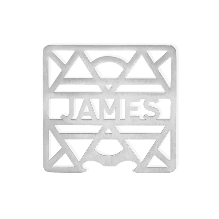 Isolated view of a personalized stainless steel coaster with 'JAMES' cutout, geometric pattern background.