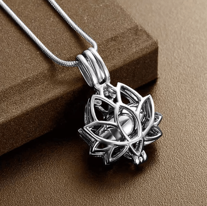 Silver lotus cremation urn necklace, displayed against a brown background.