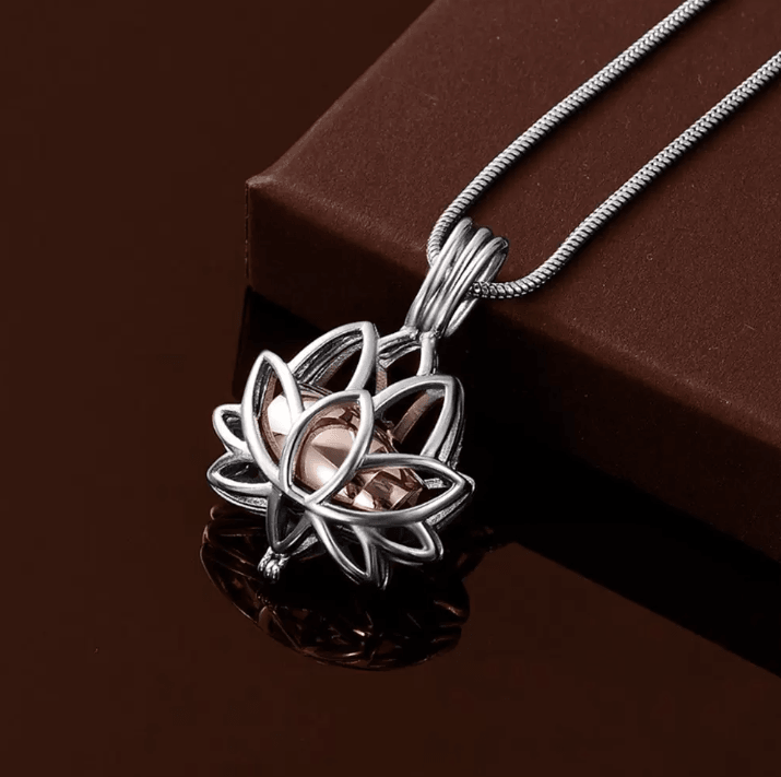 Silver lotus cremation urn necklace with a rosegold center, elegantly reflecting on a dark surface.